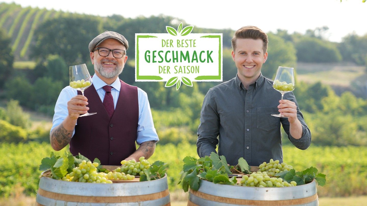 Hier sieht man zwei Sommeliers die sich gegenseitig zuprosten mit Trauben in den Gläsern