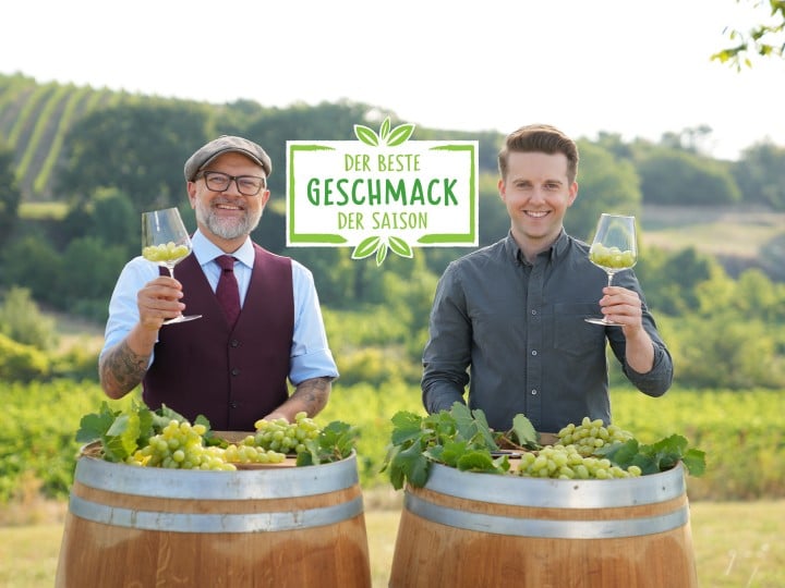 Hier sieht man zwei Sommeliers die sich gegenseitig zuprosten mit Trauben in den Gläsern