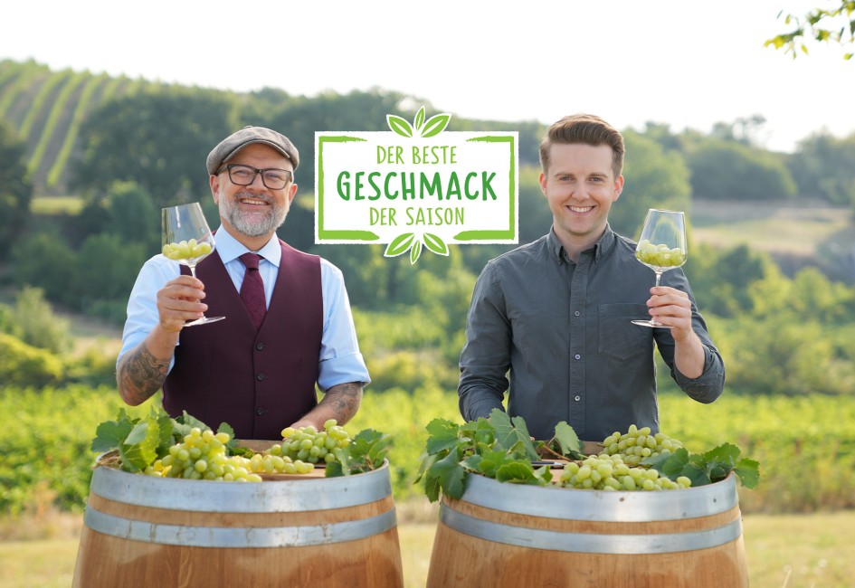 Hier sieht man zwei Sommeliers die sich gegenseitig zuprosten mit Trauben in den Gläsern