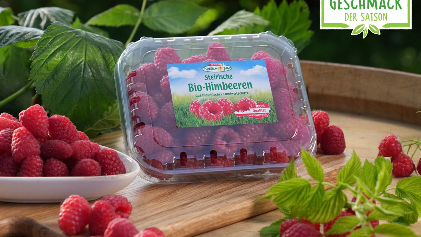 Hier sieht man die SPAR Natur*pur Bio-Himbeeren verpackt und lose auf einem Holztisch liegen