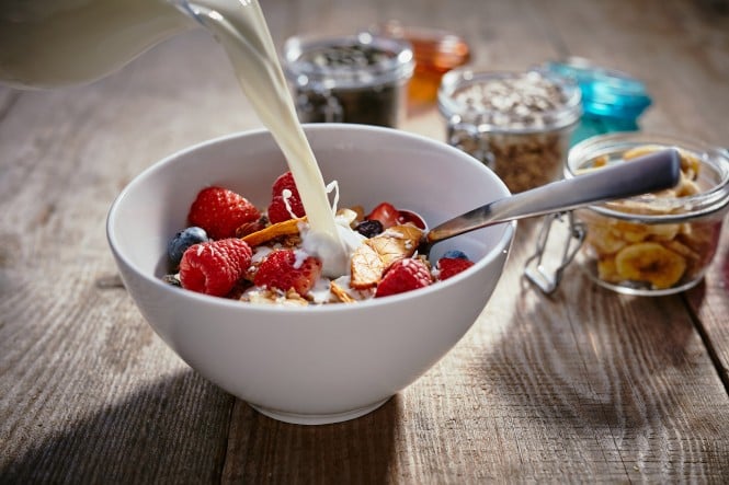 Frisches Müsli mit Beeren und Nüssen, serviert mit Milch in einer weißen Schale