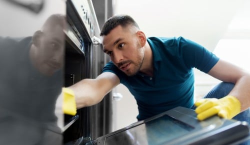 household and people concept - man wiping table with cloth cleaning inside oven at home kitchen