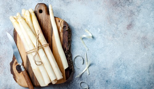 Bunch of raw white asparagus served on wooden board with knife. Top view, copy space
