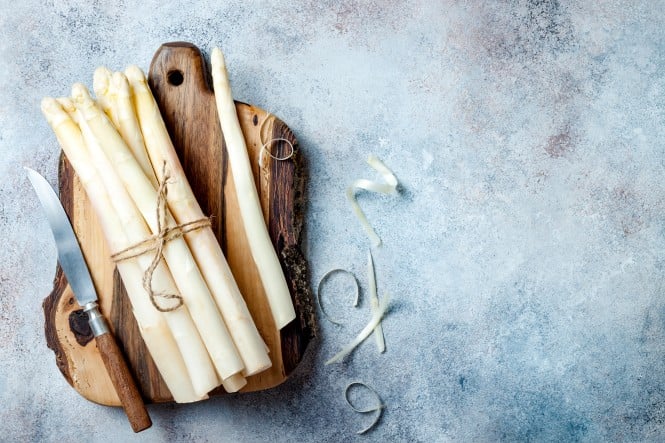 Bunch of raw white asparagus served on wooden board with knife. Top view, copy space