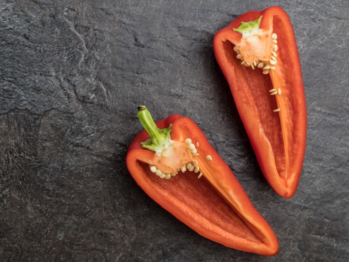 Aufgeschnittene kleine rote Spitzpaprika auf Schieferplatte 