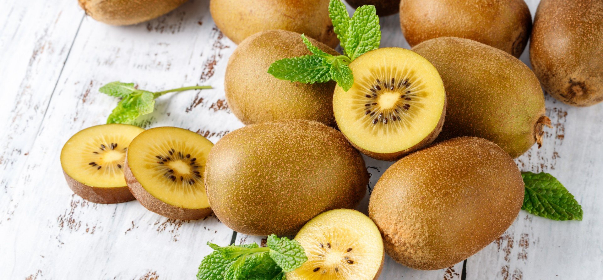 Fresh kiwi gold fruits with mint leaves scattered on rustic wooden table Fresh kiwi gold fruits with mint leaves scattered on rustic wooden table