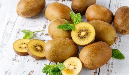 Fresh kiwi gold  fruits with mint leaves scattered  on rustic wooden table