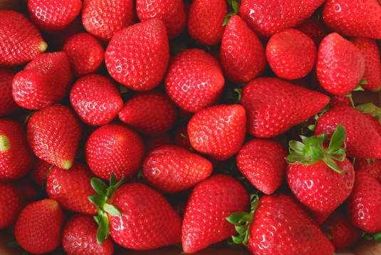 Many strawberries of faded red colour and different sizes on the local farmer market in Spain