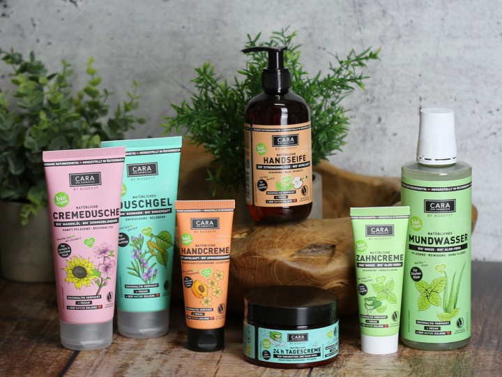 Cara by Nussyy Naturkosmetik, Produkte auf Holzplatte mit Pflanzen dekoriert