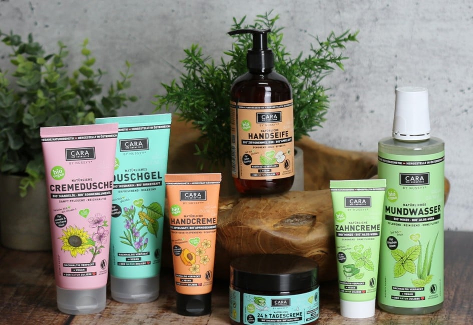 Cara by Nussyy Naturkosmetik, Produkte auf Holzplatte mit Pflanzen dekoriert