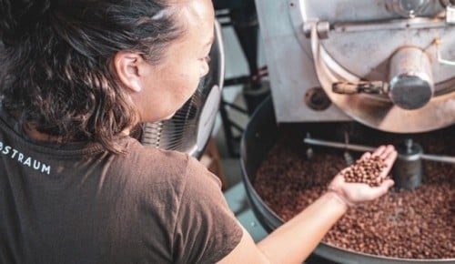 Eine Frau mit dunkel kurzen Haaren kontrolliert die gerösteten Kaffeebohnen in der Maschine
