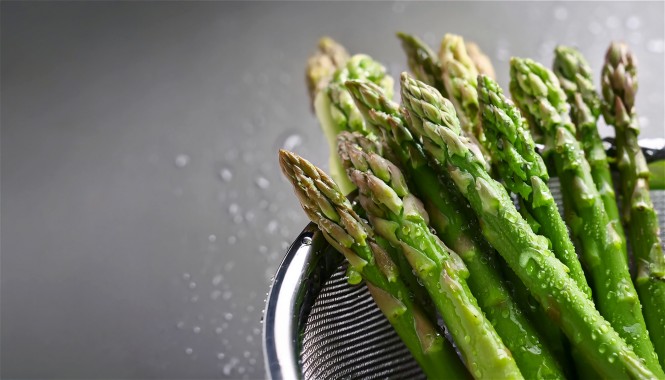 Grüner Spargel in einem Sieb vor grauem Hintergrund